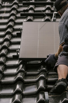 Worker places solar panel on tiled roof during modernization