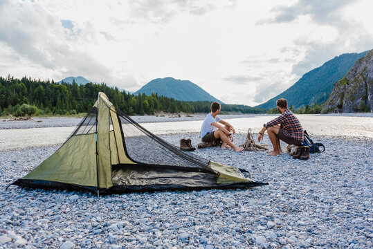 Germany, Bavaria, two hikers camping on gravel bank looking at view