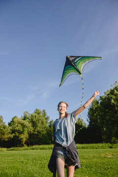 Happy girl runs outdoors flying a kite in a sunny summer field
