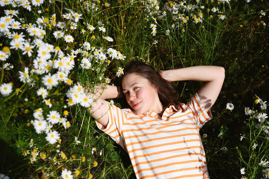 Smiling young woman in striped shirt lies in a summer daisy field