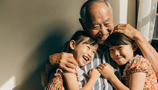 Elderly Asian grandfather hugging two young granddaughters, smiling together in warm sunlight, family love and happiness at home, joyful bonding moment, cheerful and affectionate expression