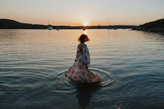 A woman spins in the Mediterranean Sea at sunset in Menorca