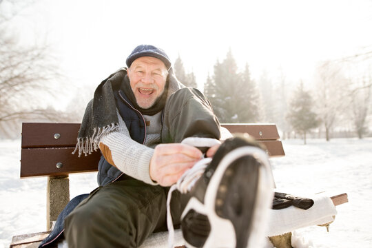 Portrait of happy senior man sitting on bench in winter landscape putting on ice skates