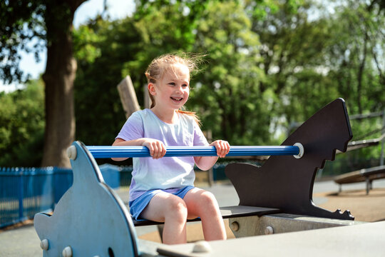 Happy girl plays on a seesaw at the outdoor playground