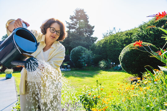 Woman waters blooming flowers in a sunny backyard garden