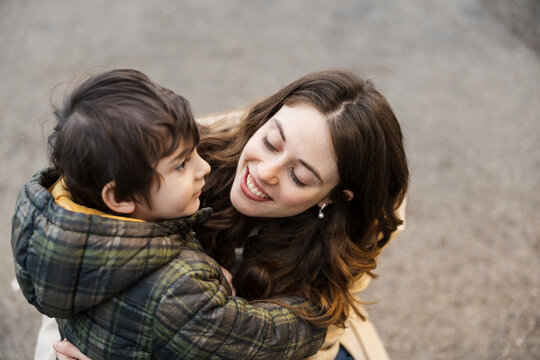 A smiling mother hugs her young son outdoors during the day