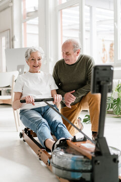 Man cheering on woman using rowing machine at home