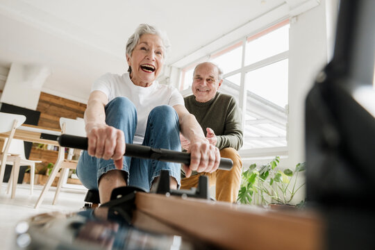 Smiling man cheers woman using rowing machine indoors