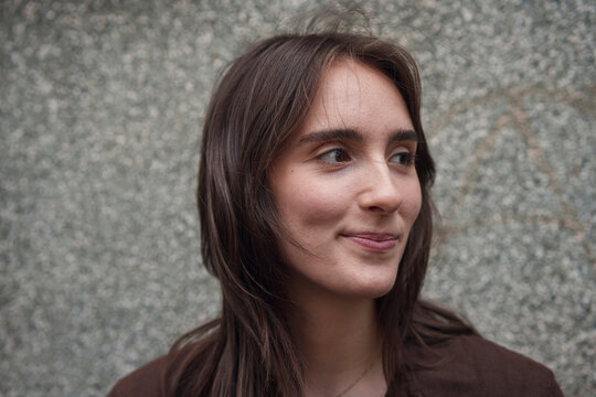 A smiling woman looks away against a gray wall