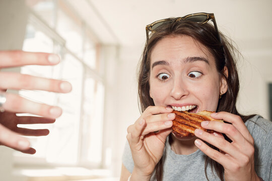 Funny woman eating a sandwich indoors while a man reaches for it