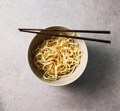 Plain cooked noodle in a bowl with chopstick on grey stone background