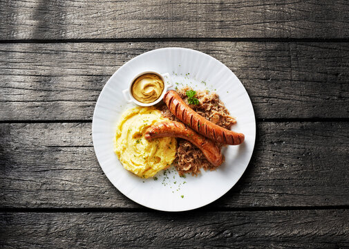 Plate of grilled bratwurst features mashed potato and sauerkraut