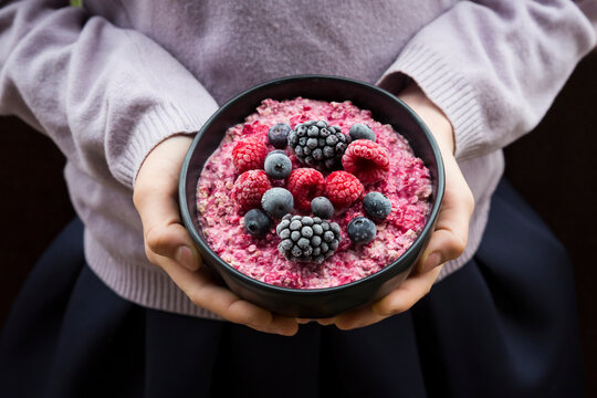 Girl holding bowl with overnight oats mit frozen berries