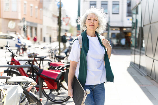Woman holds a skateboard while walking in the sunny city