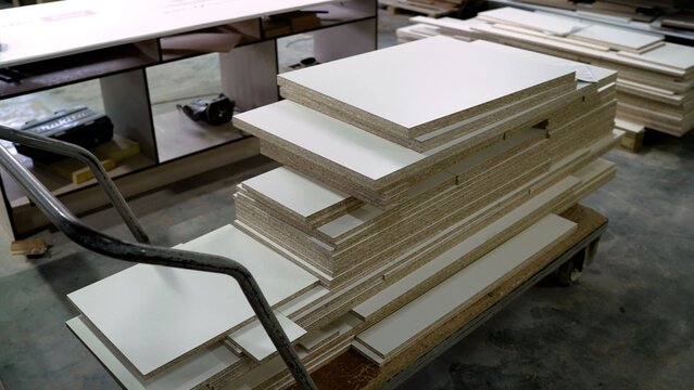 Stacks of white laminated particle board on industrial trolley in furniture manufacturing workshop, woodworking and assembly process