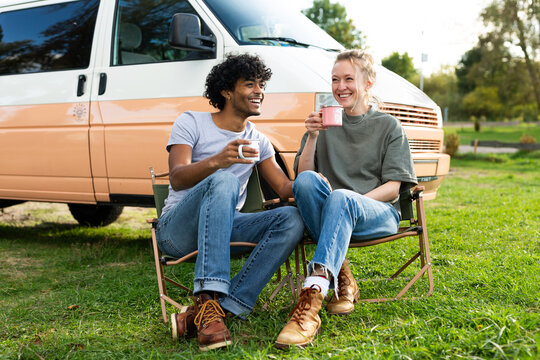 Happy couple drinks coffee outside their camper van in nature