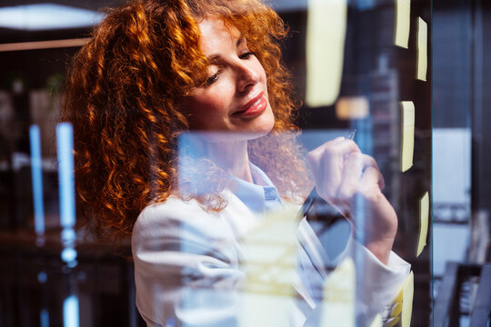 Smiling businesswoman writing on glass board with sticky notes