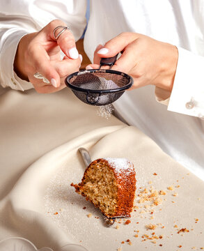 Mature woman sifting powdered sugar over a slice of lemon cake