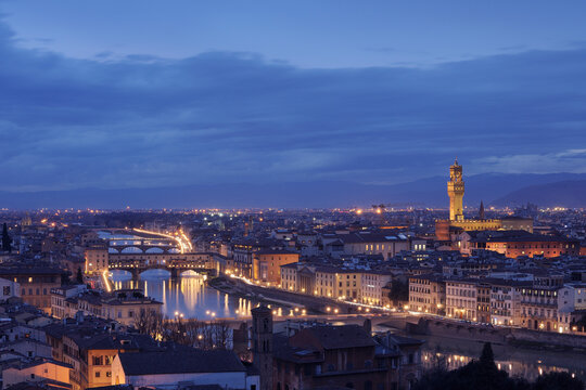 The Arno River reflects city lights in Florence at dusk