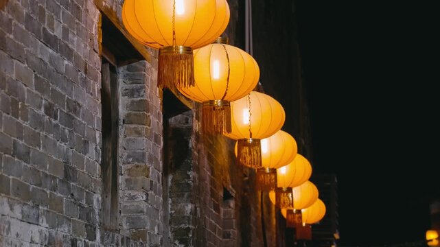 Glowing Orange Chinese Lanterns Hanging on Brick Wall at Night
