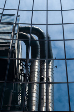Industrial pipes behind a modern glass facade combine architecture infrastructure and technology with urban reflection in a graphic vertical composition