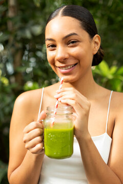 A smiling woman drinks a healthy green smoothie outdoors