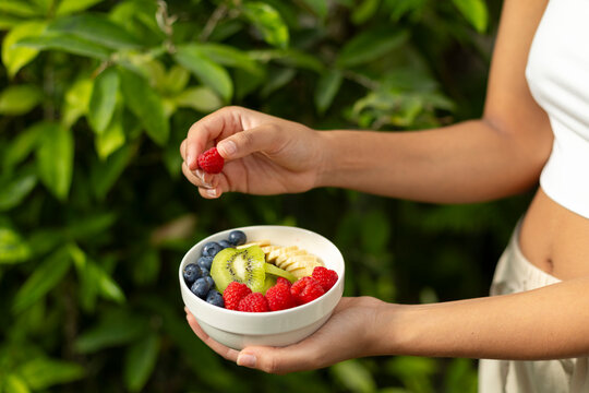Woman holds a healthy fruit bowl with fresh fruit outdoors