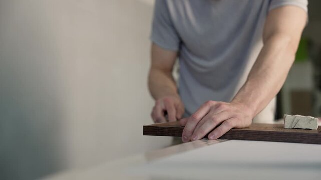 Carpenter's hands carefully finishing edge of dark wood board with hand tool in workshop, skilled manual labor