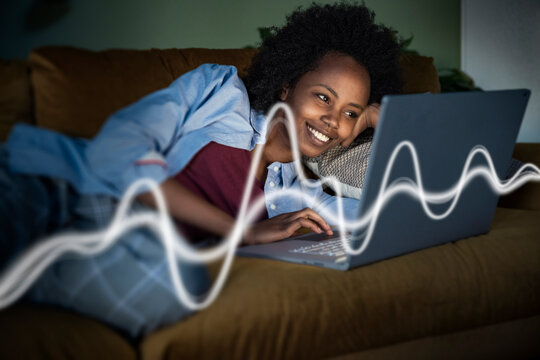 Smiling woman uses laptop with glowing data waves on couch at night