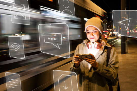 Smiling woman uses smartphone in city at night with digital icons