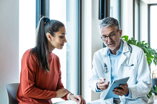 Male doctor explains treatment to female patient on digital tablet