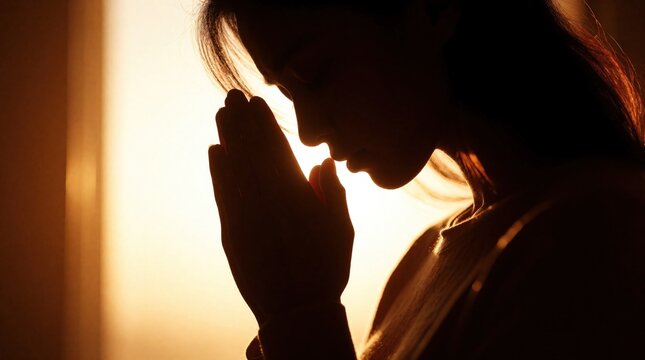 Silhouette of young woman praying with hands together in warm sunset light. Female believer shows faith, devotion in peaceful moment. Religious person seeks spiritual connection, hope, divine grace