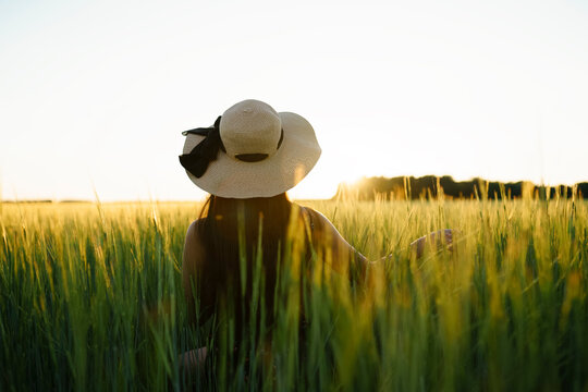 Woman wearing a straw hat touches wheat in a field at sunset
