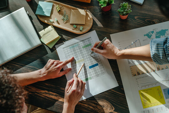 Hands of colleagues analyzing business graphs during office meeting