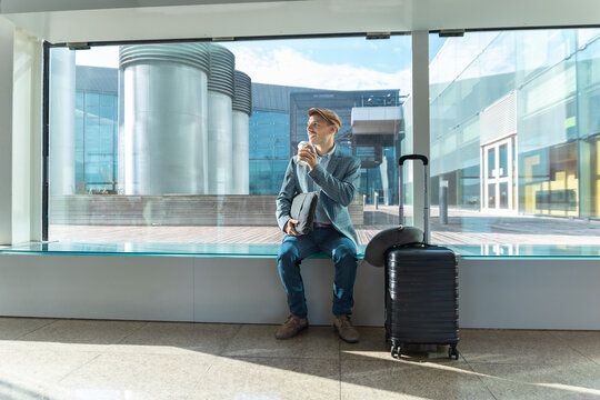 A smiling male passenger drinks coffee by the window at the airport