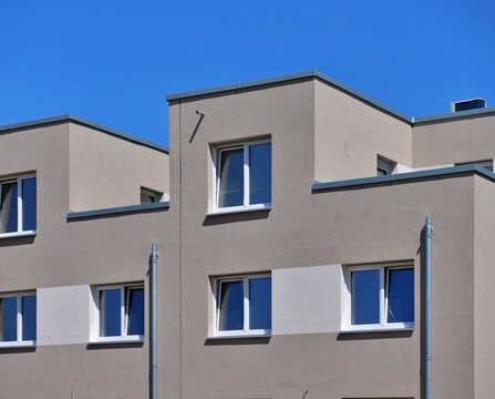 Modern Apartment Building Facade with Geometric Cubic Design, Rectangular Windows, and Plaster Finish Under Bright Blue Sky