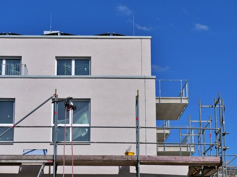 Construction Scaffolding Mounted on Modern Residential Apartment Building Facade Under Clear Blue Sky for Renovation and Finishing Works