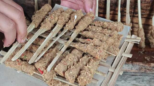 Close up of hands arranging raw traditional Balinese sate lilit skewers made of minced meat on flat bamboo sticks