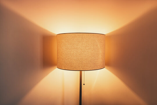 Floor lamp with linen shade casting warm glow on interior wall at night. Cozy home lighting concept.