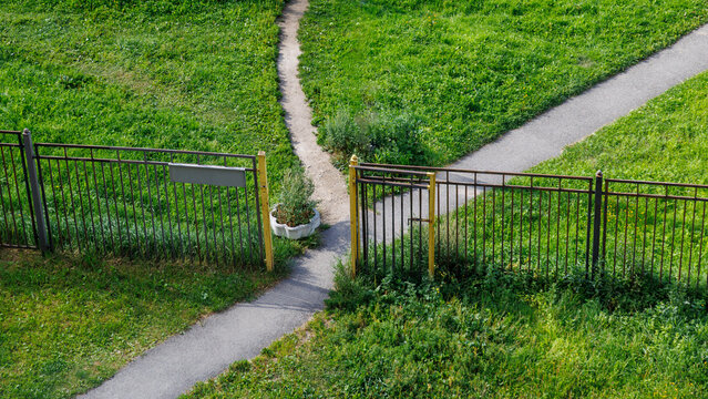 Grassy path splits at wooden gate with metal fencing