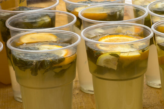 Clear plastic cups hold chilled lemonade with slices and herbs
