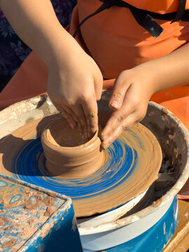 Child shapes clay on a pottery wheel