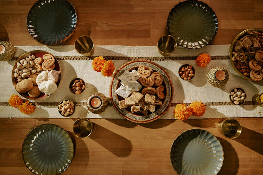 Top view of festive dining table displaying traditional sweets, flowers and candles for cultural holiday celebration. Visual ideal for ethnic food marketing and seasonal advertising