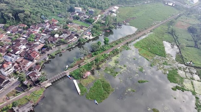 Beautiful aerial drone view of the Blue Bridge (Jembatan Biru Sumurup) at Rawa Pening lake with local village houses in Semarang, Central Java, Indonesia.