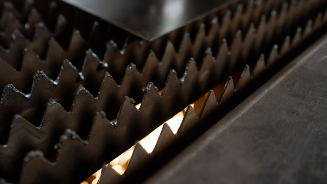 Industrial detail of cnc laser cutting machine bed with toothed metal slats and steel sheet, precision metalworking