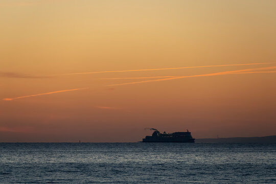 Luc-Sur-Mer, France - 08 08 2026: Fishermen's Pier. Colorful sunrise over the sea from the beach and a cruise ship far away