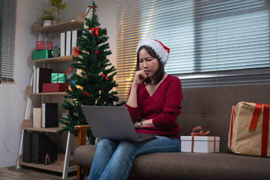 Asian woman wearing a Santa hat looking at a laptop with a concerned expression on a sofa