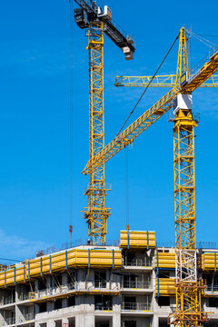 Cranes rise above a concrete building at a construction site where urban architecture and development shape the structure against the sky