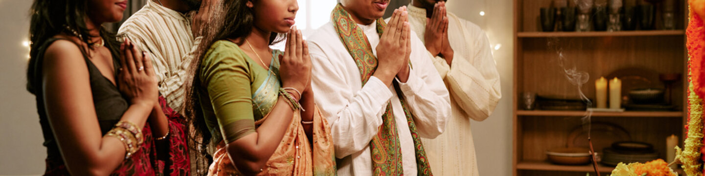 Indian young adults standing with folded hands praying together during cultural holiday ceremony. Visual ideal for multicultural festival advertising campaigns
