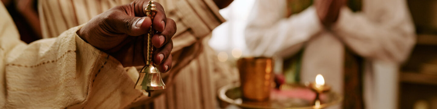 Header close up of Indian young adult hand ringing brass prayer bell during traditional religious celebration. Useful for holiday advertising and cultural diversity campaigns